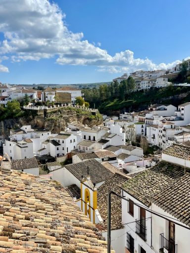 Vista panorámica de un pueblo blanco, con montañas y nubes en el cielo despejado.