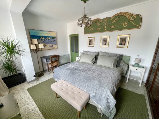 Habitación luminosa con cama grande, sillón, mesa y plantas decorativas.