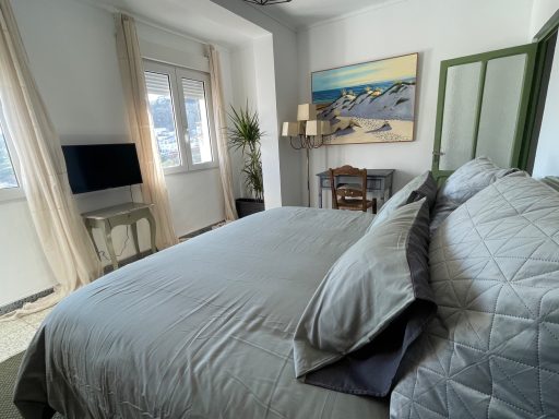 Dormitorio luminoso con cama grande, mesa, televisor y cuadro decorativo en la pared.