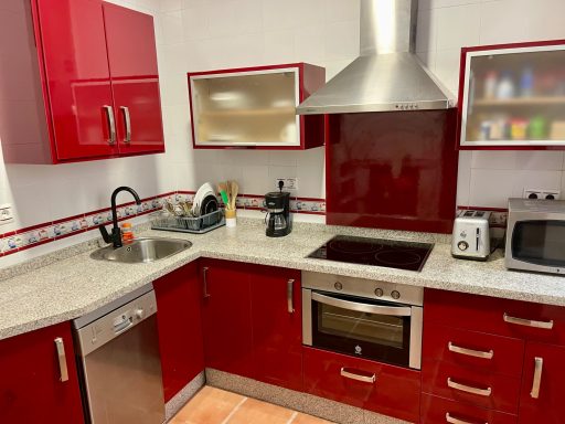 Cocina moderna con mobiliario rojo, encimera clara y electrodomésticos metálicos.