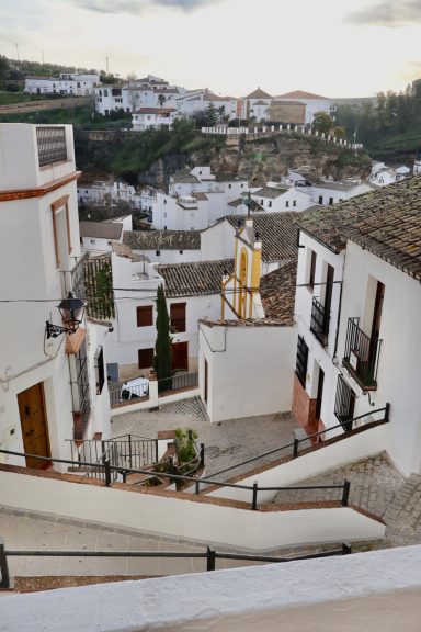 Calles empinadas y blancas en un pueblo andaluz con vistas a casas en la colina.