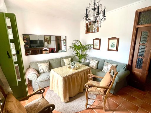 Sala de estar con sillones, mesa, plantas y lámpara de araña en un ambiente acogedor.