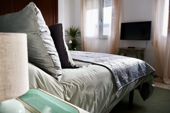 Habitación acogedora con cama, almohadas decorativas, televisión y luz suave.