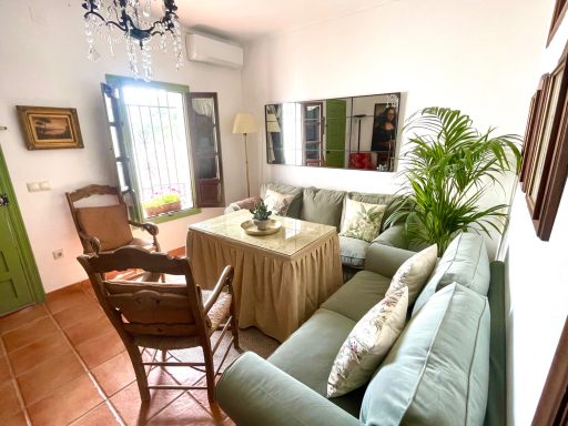 Sala de estar luminosa con sofá verde, mesa con mantel y plantas decorativas.