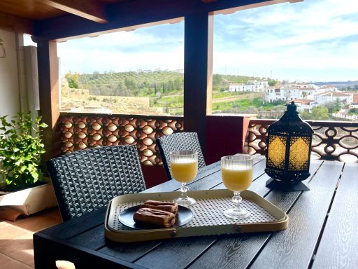 Bandeja con dos bebidas y un pastel en una terraza con vista al paisaje.