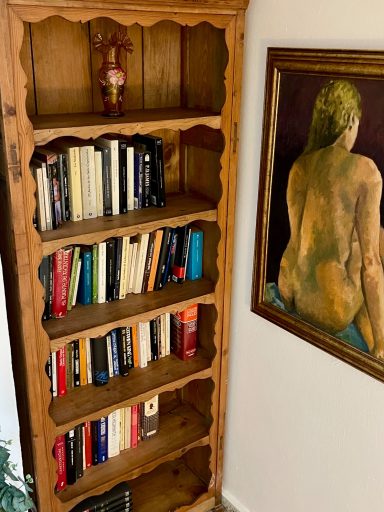 Estantería de madera con libros y una pintura de una figura desnuda al fondo.