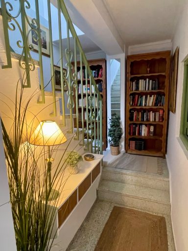 Escalera con barandilla verde, estantería, planta y lámpara de pie en un ambiente acogedor.